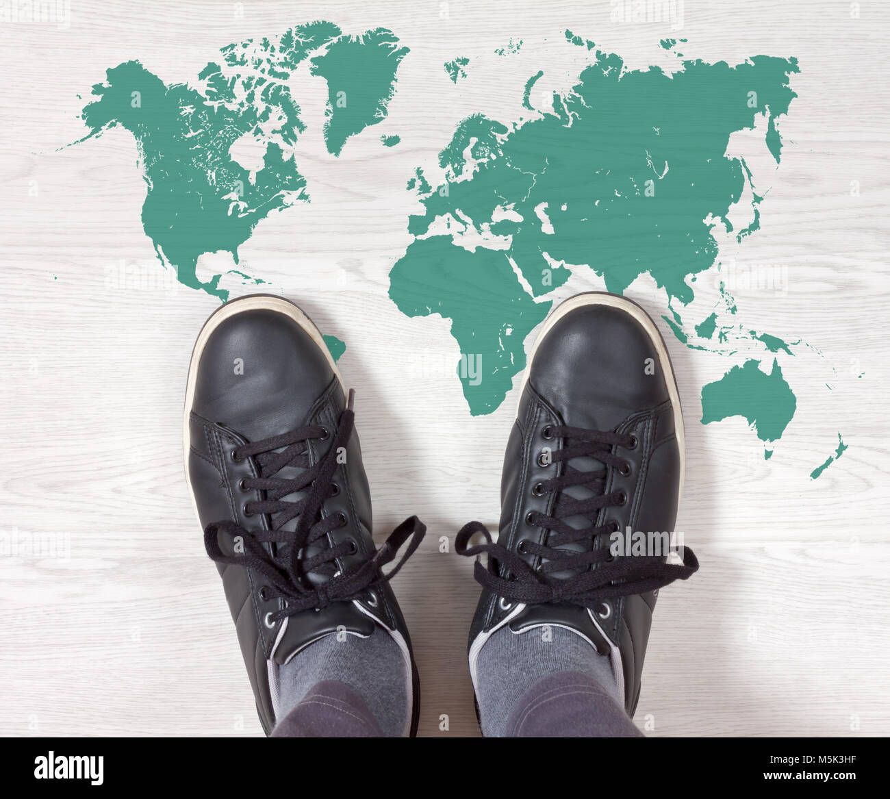 Black sneakers standing on a white wooden floor with a turquoise world map outline painted on it Stock Photo
