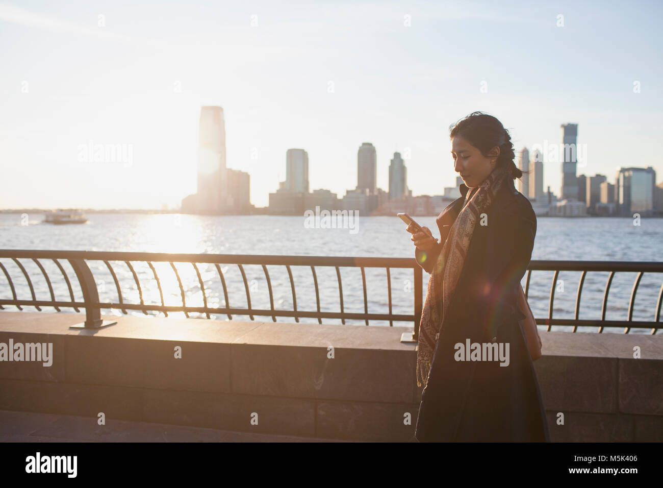 Young asian business woman looking at her smartphone standing on river romenade Stock Photo