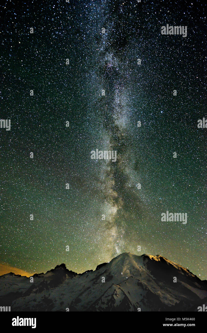 The Milky Way rises above the summit of Mount Tahoma, also known as Mount Rainier, at 2 am on July 25, 2017. The headlamps of climbers can be seen. Stock Photo