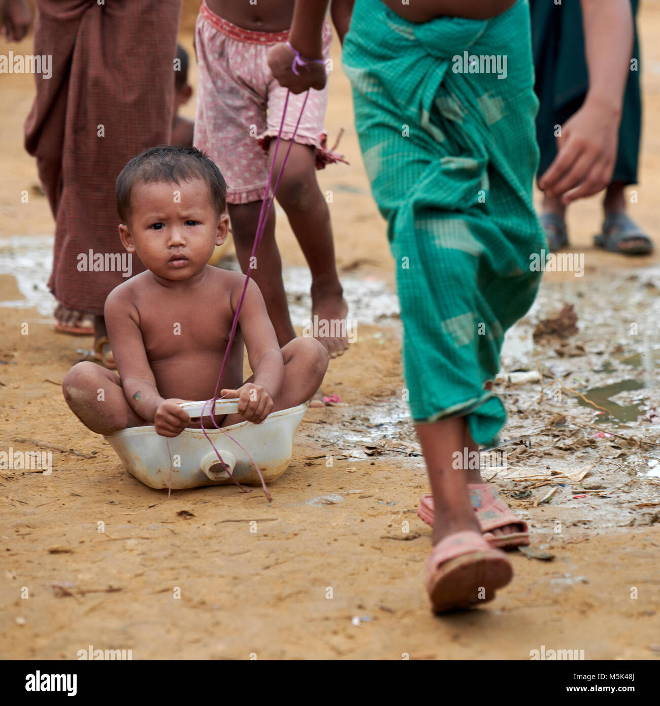 A Rohingya refugee child holds on tight as another child pulls them along the dirt street in the sprawling Kutupalong Refugee Camp in Bangladesh. Stock Photo