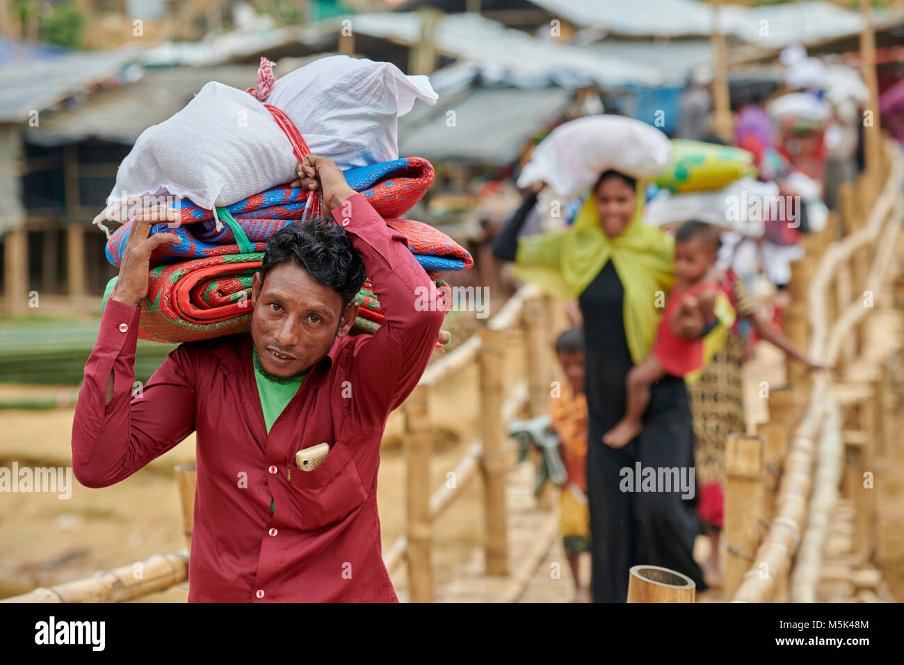 Carrying emergency shelter materials and food, Rohingya refugees cross a rickety foot bridge in the sprawling Kutupalong Refugee Camp in Bangladesh. Stock Photo