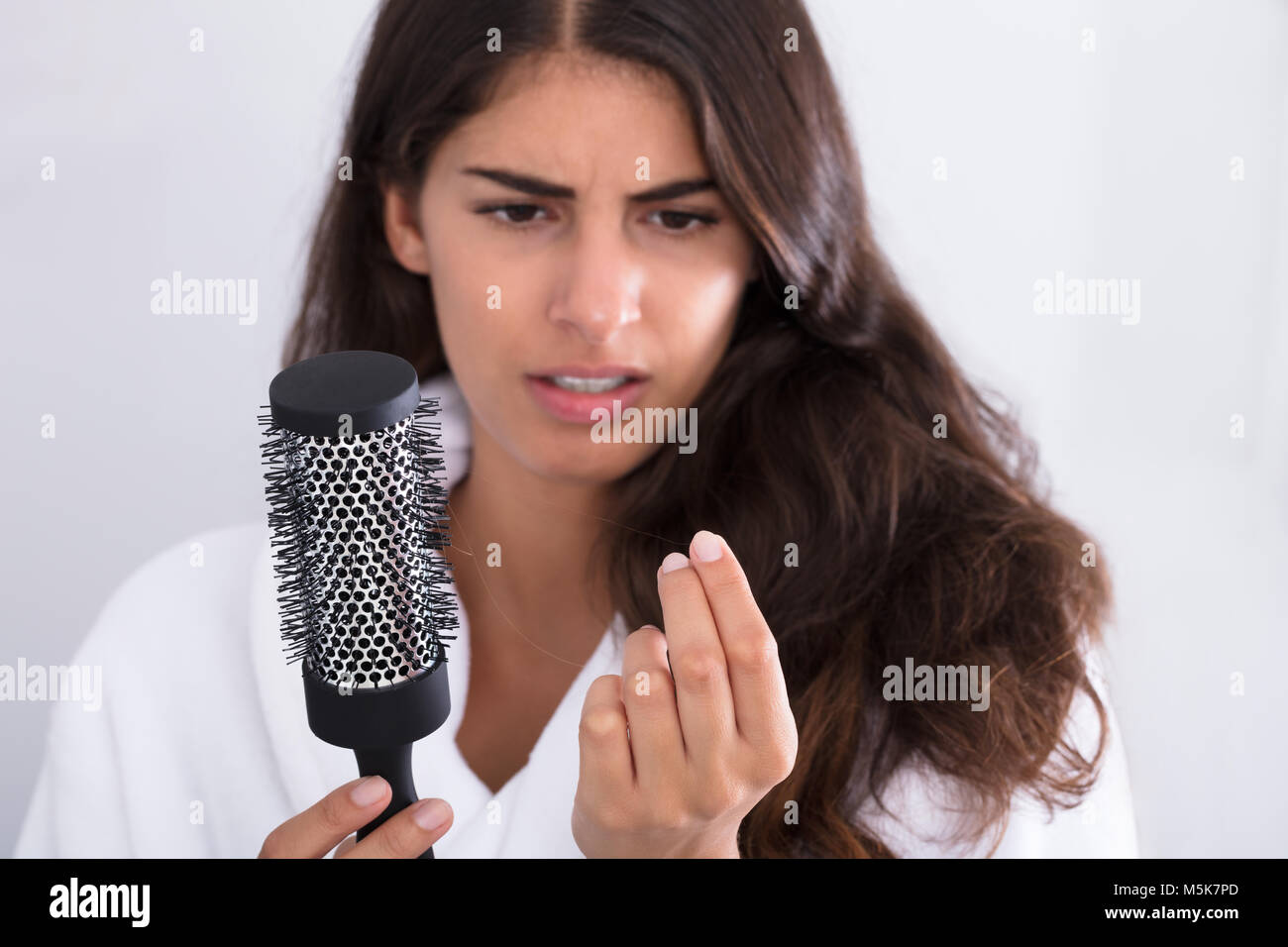 Young Woman In Bathrobe Holding Comb Looking At Hair Loss At Home Stock Photo