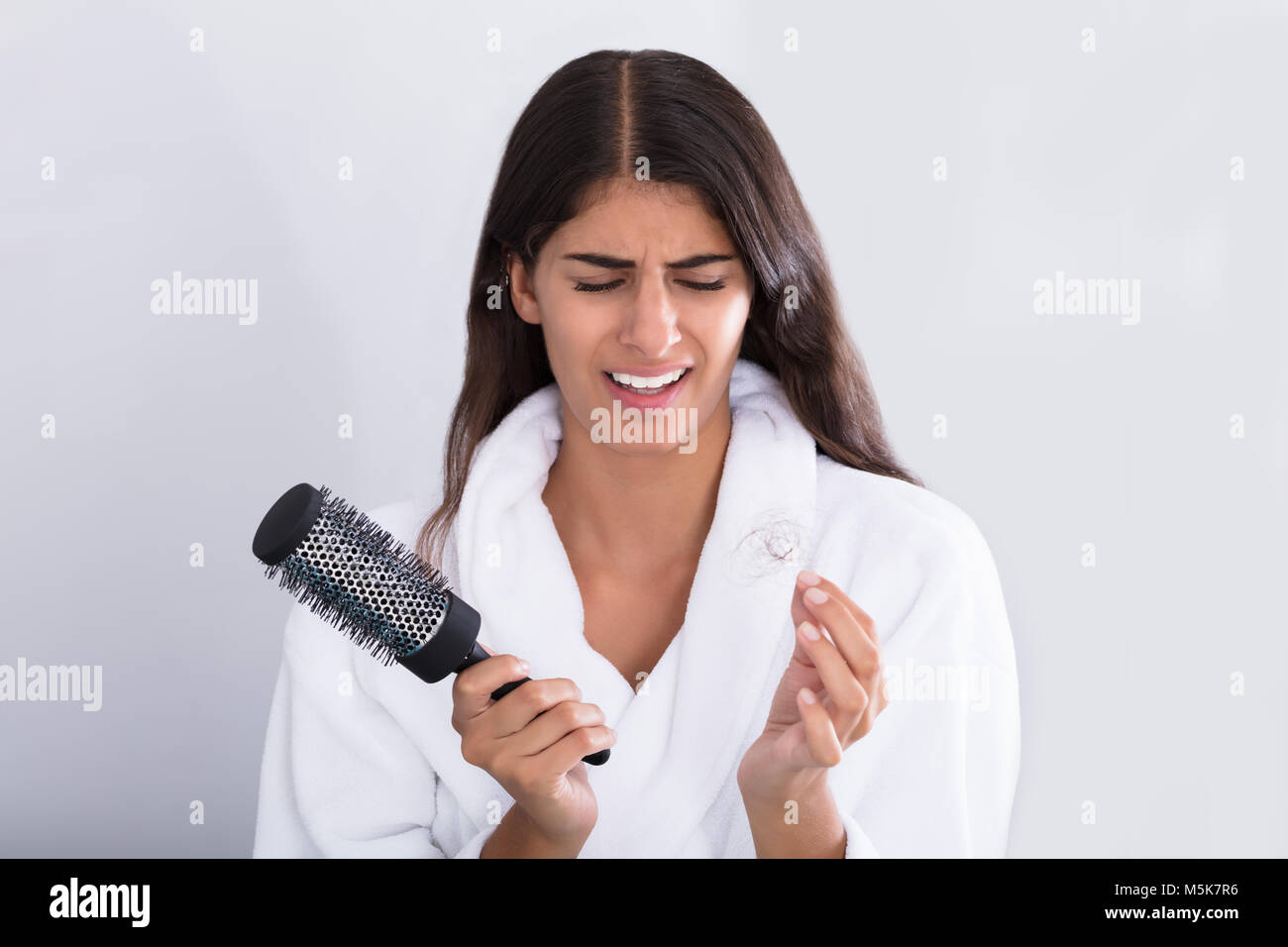 Shocked Young Woman In Bathrobe Holding Comb While Looking At Hair Loss At Home Stock Photo