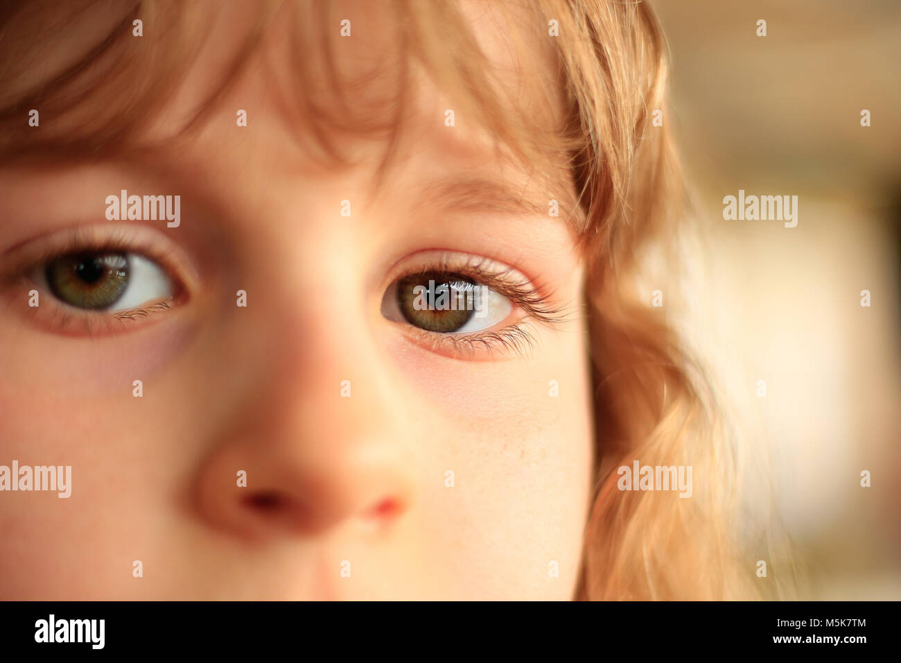 Partial face of a young girl with large  green eyes and light hair; light background Stock Photo