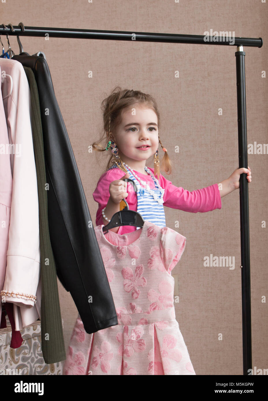 Little girl trying on a new dress. Small girl chooses dress. Little girl and clothes hangers shopping. Clothes rack Stock Photo