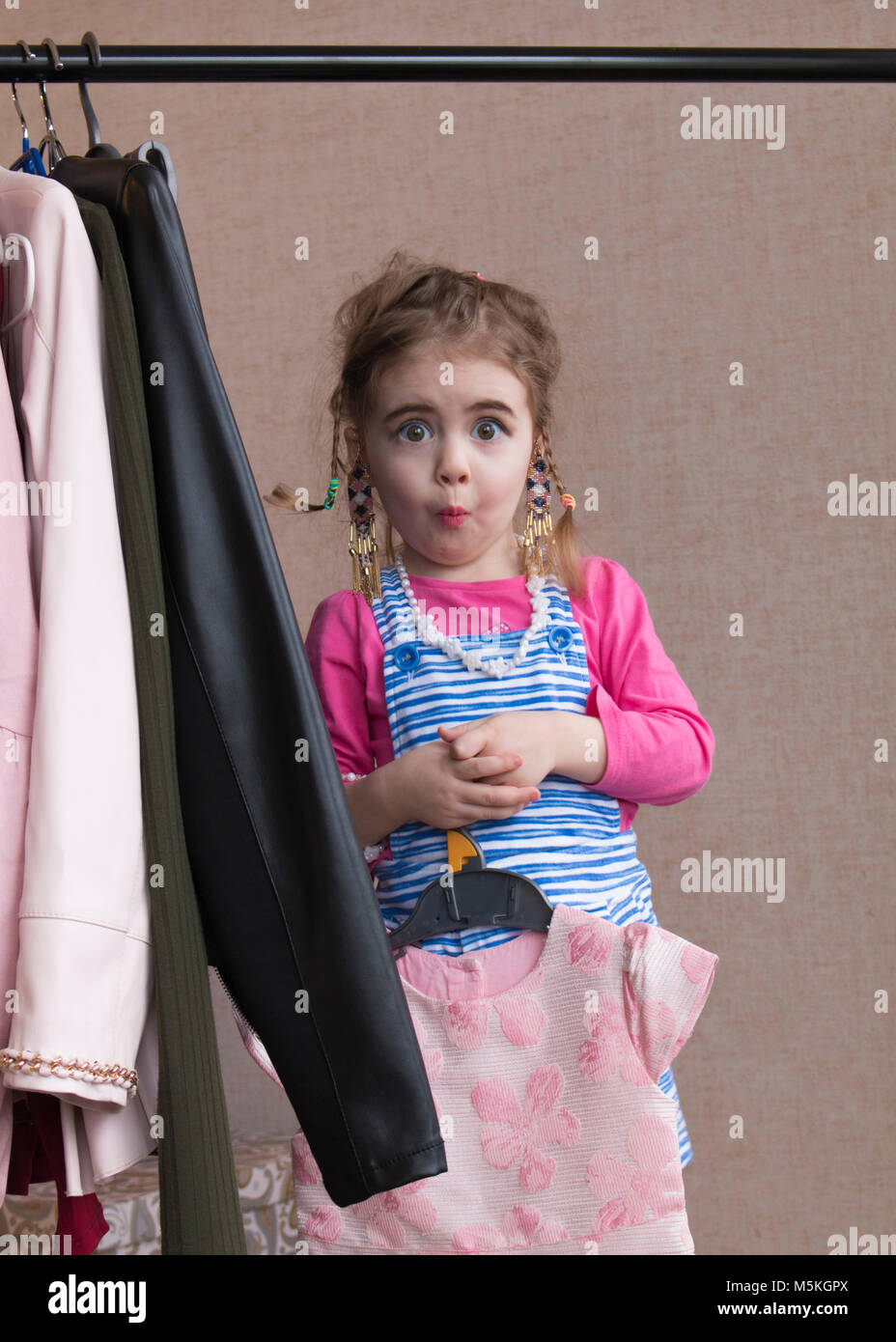 Little girl trying on a new dress. Small girl chooses dress. Little girl and clothes hangers shopping Stock Photo