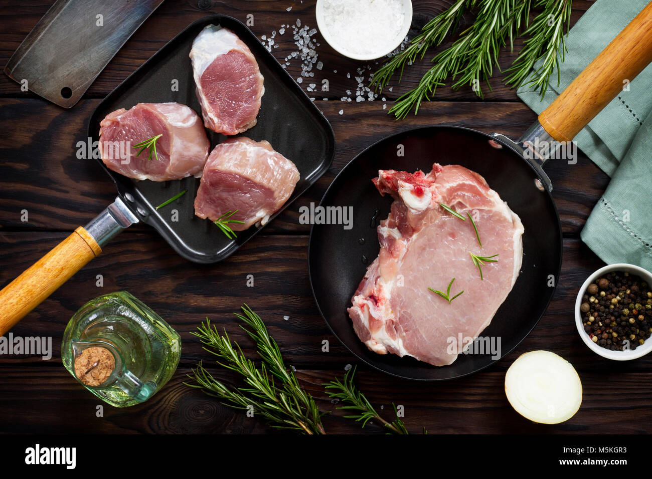 Fresh various meat. Raw pork steak and cutlets on a cast iron frying pan, spices and fresh rosemary on a kitchen wooden table. Flat lay. Top view. Stock Photo