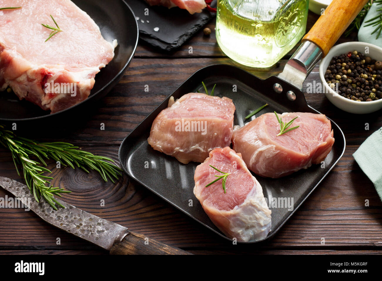 Fresh various meat. Raw pork steak and cutlets on a cast iron frying pan, spices and fresh rosemary on a kitchen wooden table. Stock Photo