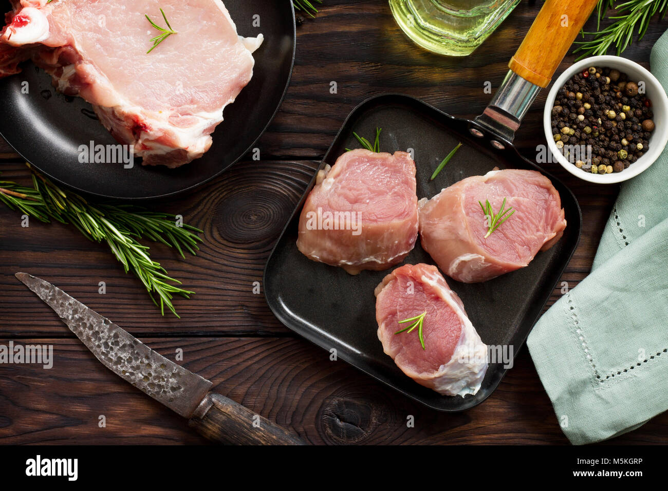Fresh various meat. Raw pork steak and cutlets on a cast iron frying pan, spices and fresh rosemary on a kitchen wooden table. Stock Photo