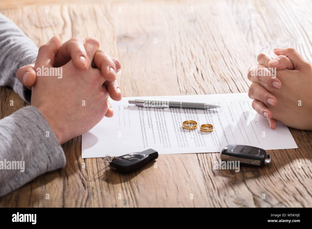 Hands On Divorce Document With Wedding Rings And Car Keys On Table