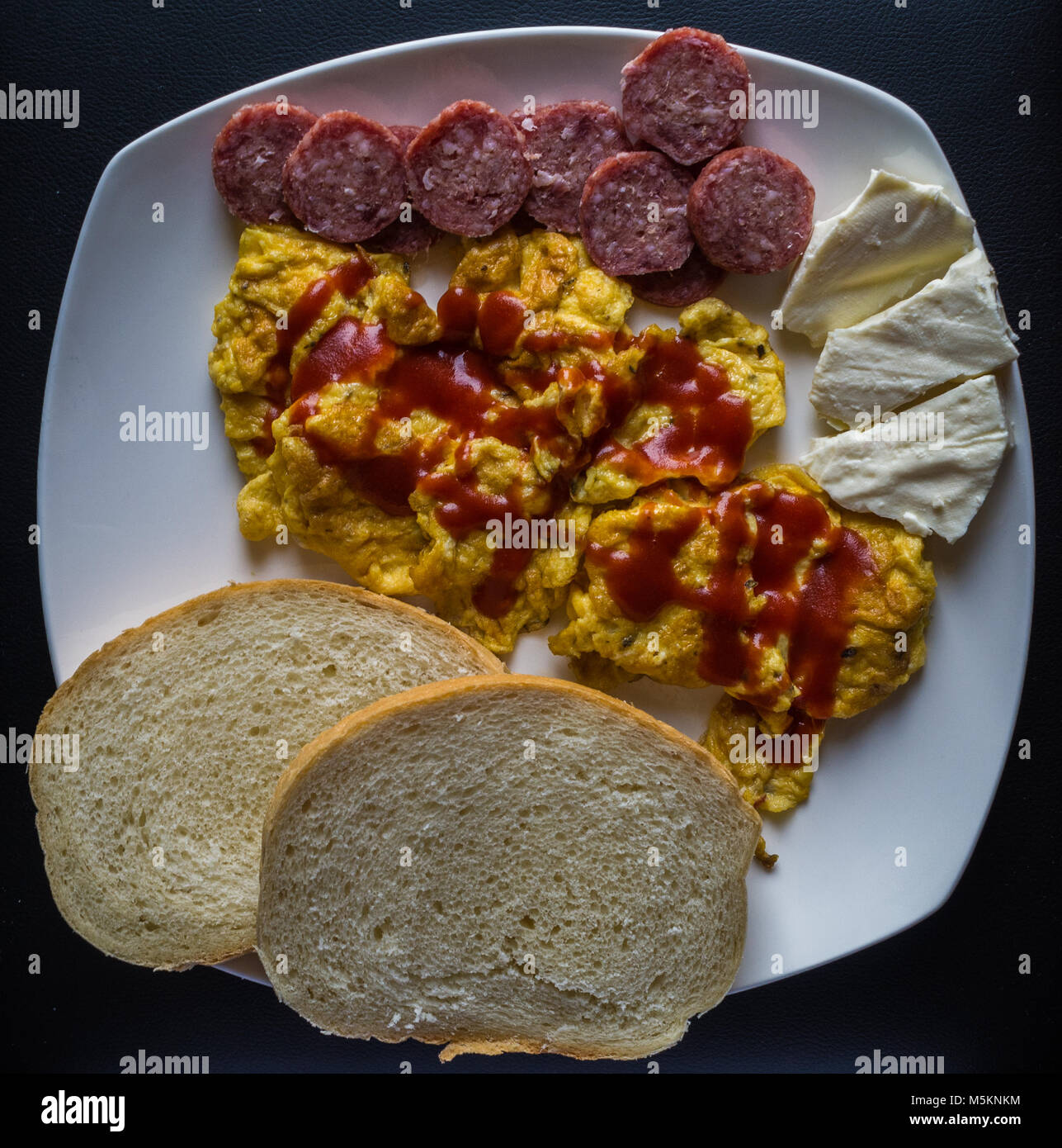 Scrambled eggs with ketchup with bread, salami and cheese Stock Photo
