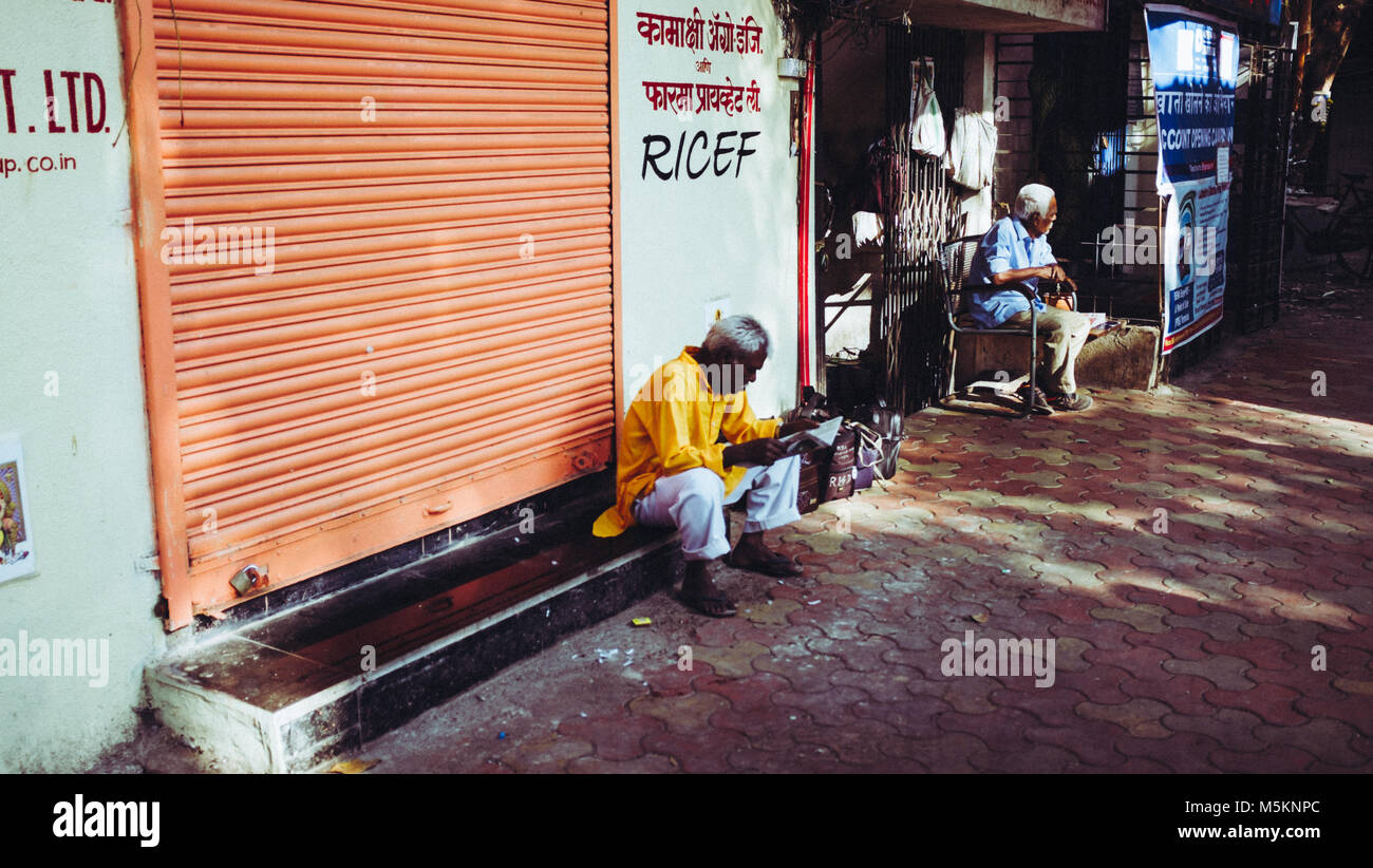 A man sitting outside a shop with the shutters down in Mumbai, India Stock Photo