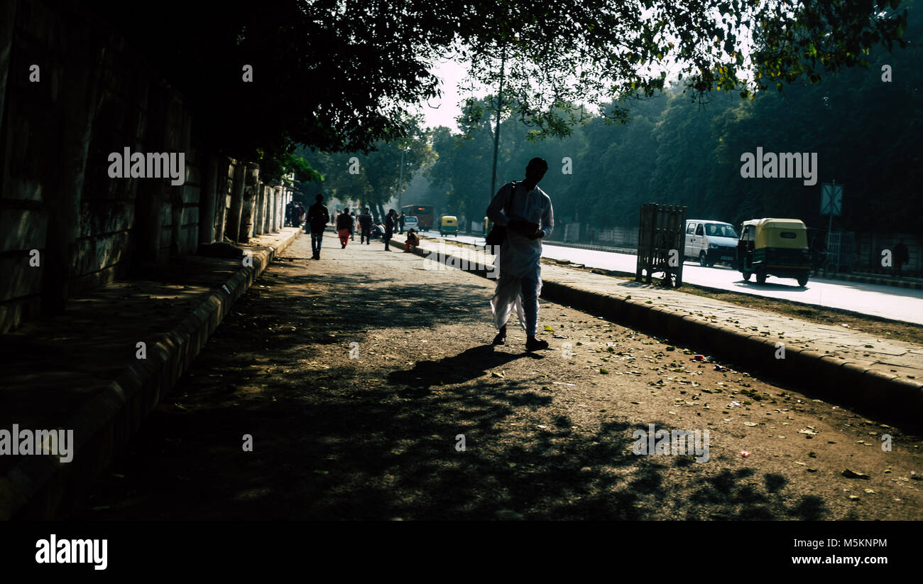 People walking and sitting along the side of the road in Delhi, India Stock Photo