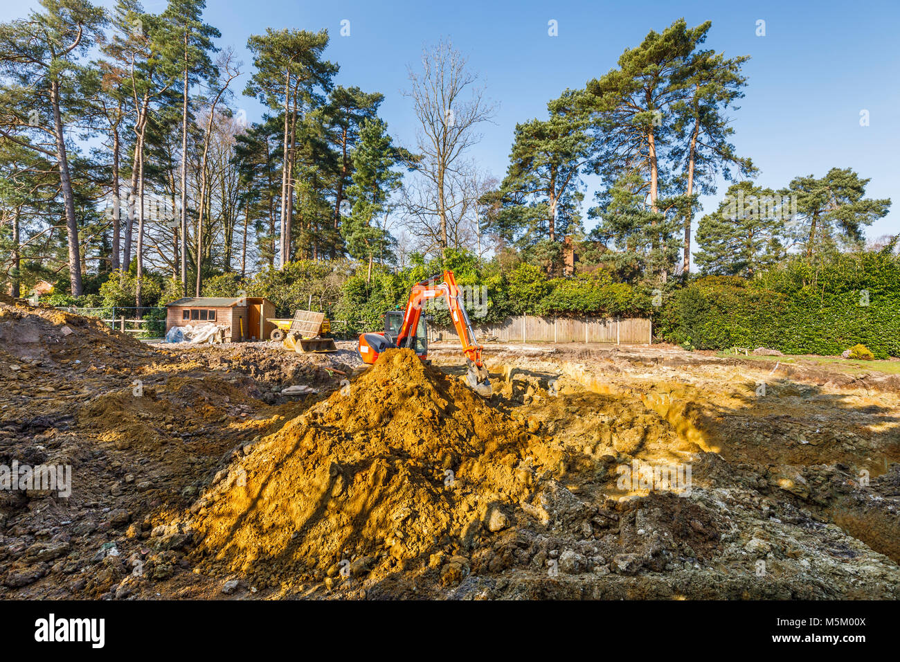 Large orange heavy plant mechanical digger parked on a construction site after digging excavations for foundations of a new residential development Stock Photo