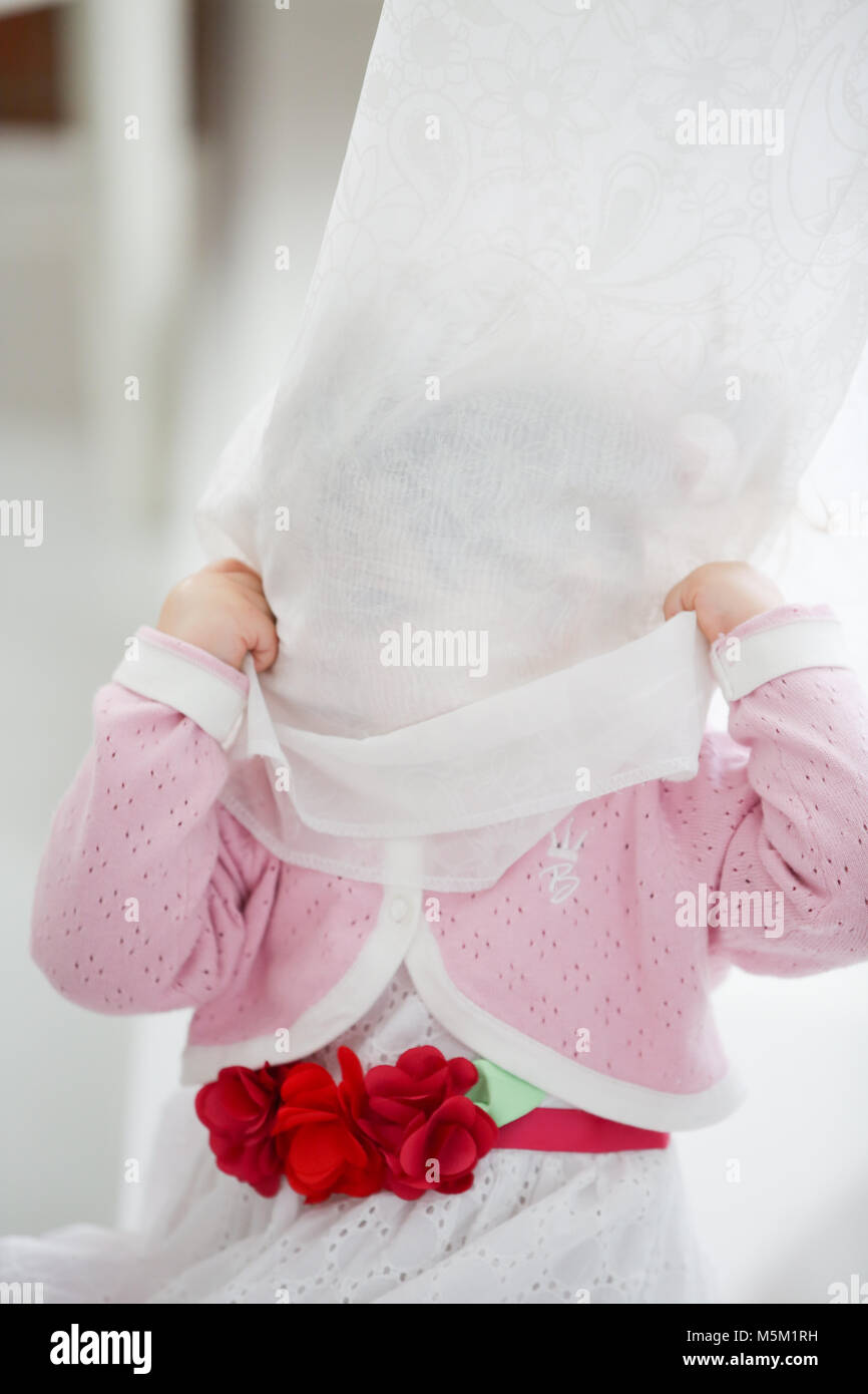 Portrait of little girl peeking from curtains at home Stock Photo