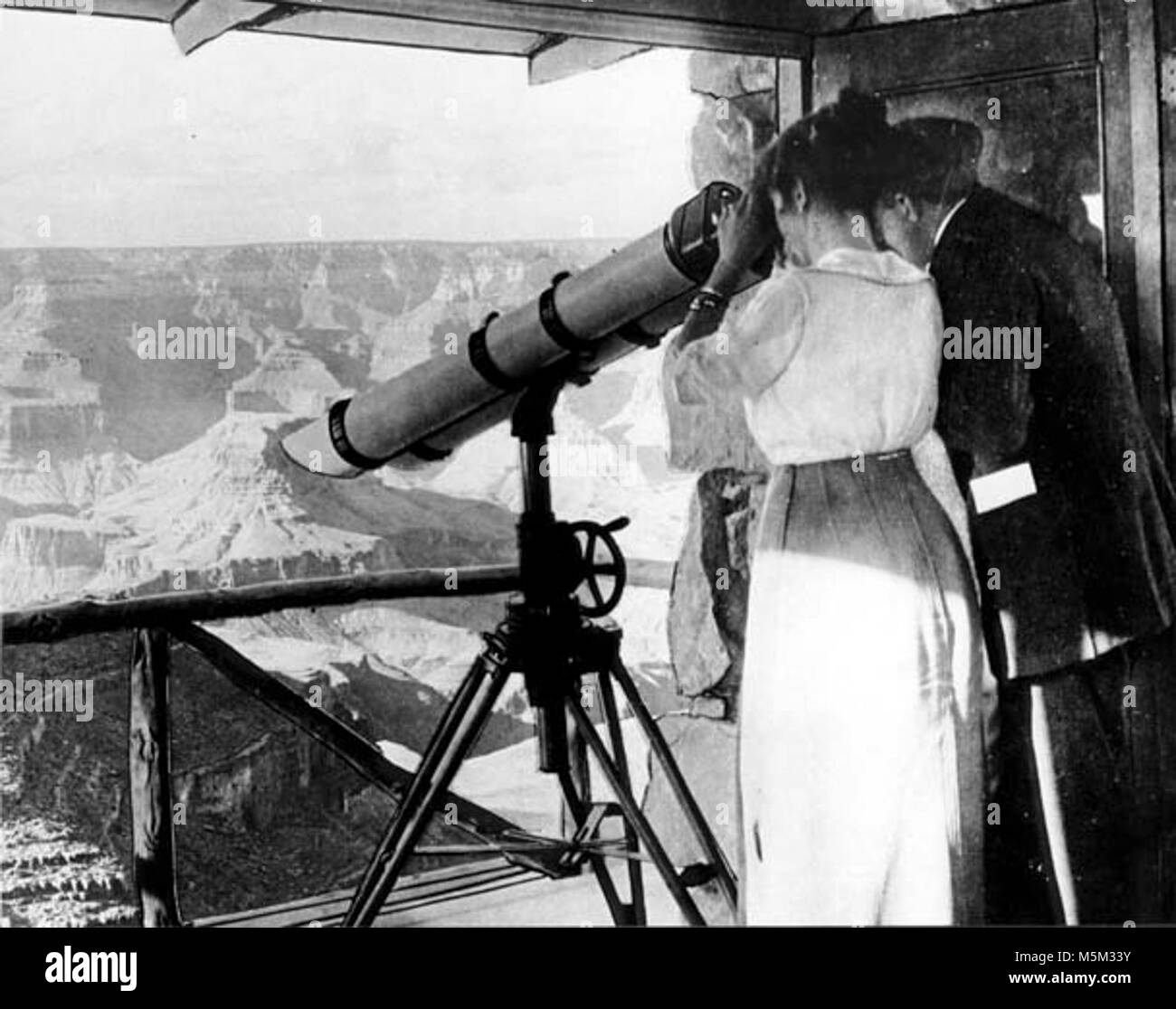 Grand Canyon Historic Lookout Studio  Interior c  . LOOKOUT STUDIO. 'IN THE TELESCOPE TOWER' (CANYON IMAGE PASTED IN WINDOW)  COUPLE VIEWING CANYON. GRCA 50633 CIRCA 1915. FRED HARVEY CO Stock Photo