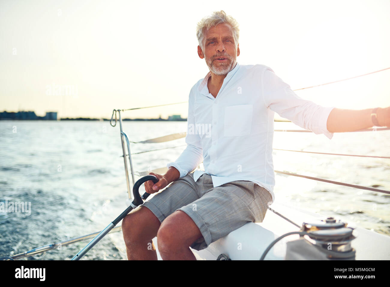 Smiling mature man sitting on the deck of his boat enjoying a sunny day ...