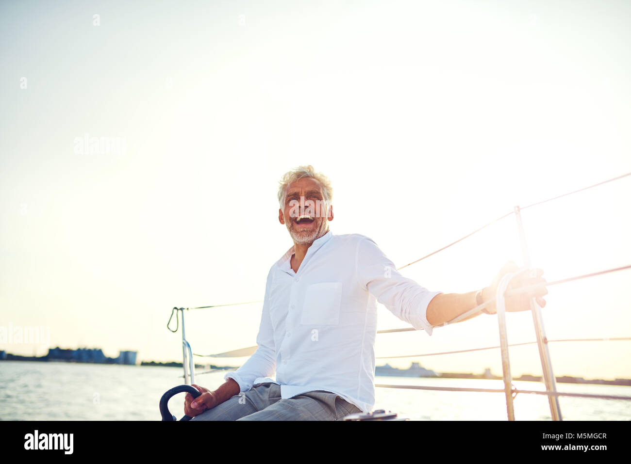 Mature man sitting on the deck of his yacht laughing while enjoying the ...