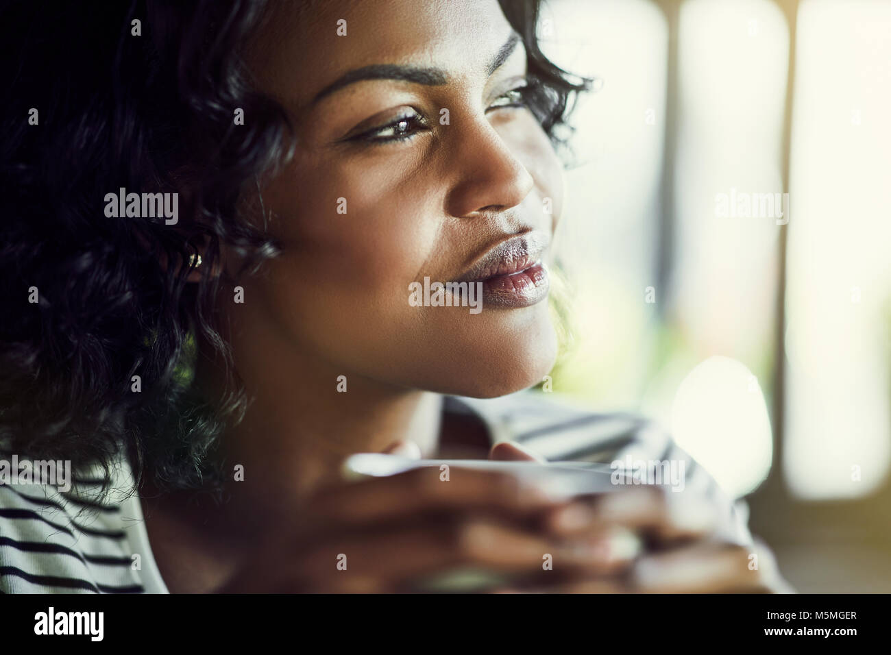 Smiling young African woman looking deep in thought while enjoying a fresh cup of coffee Stock Photo