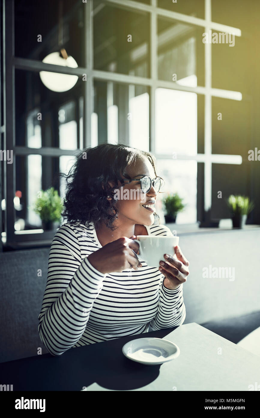 Smiling young African woman sitting at a table in a cafe enjoying a ...