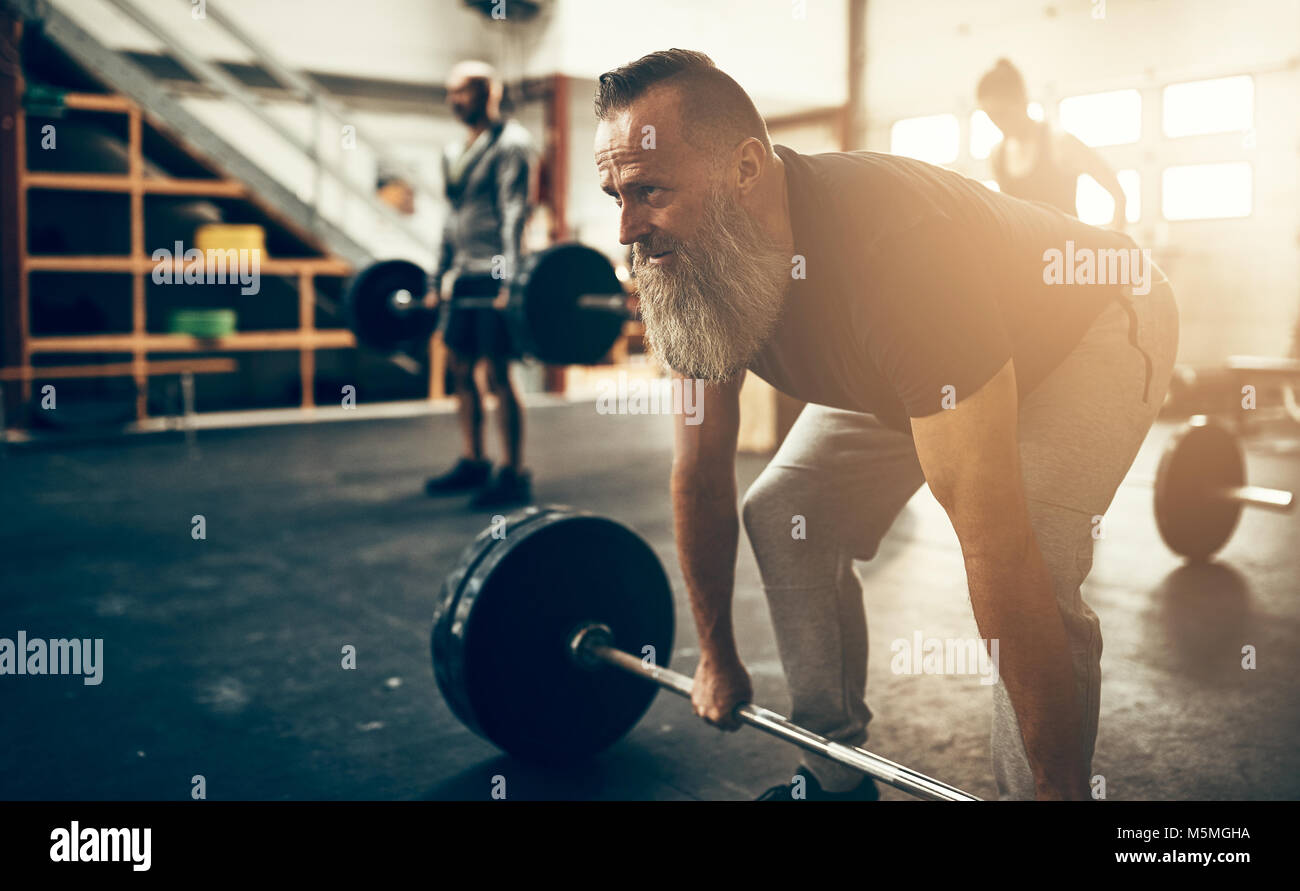 Mature man with a beard wearing sportswear preparing to lift weights while  working out in a gym Stock Photo - Alamy