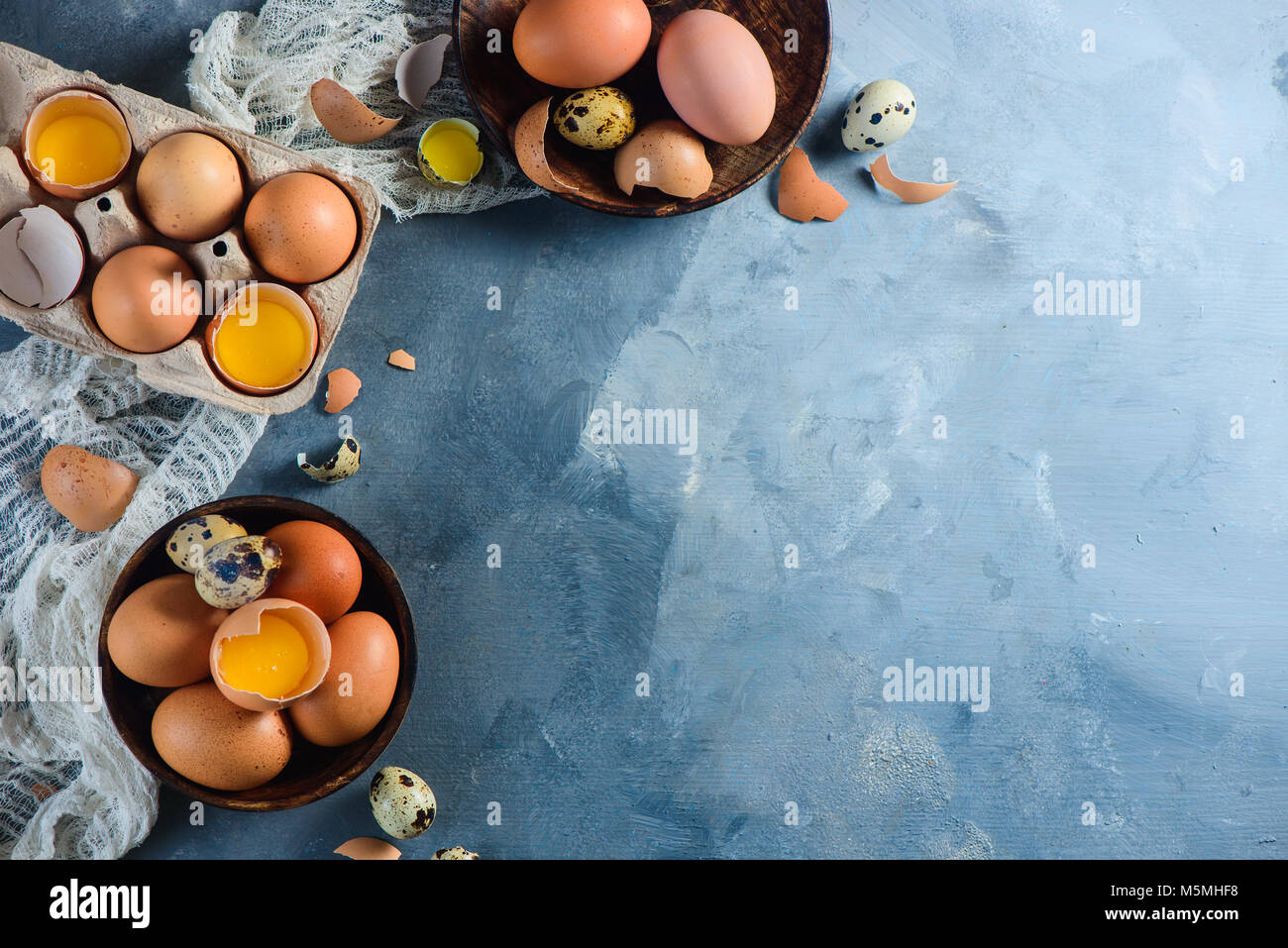 Header with raw brown hen and quail eggs, whole and broken, on a wooden dish and carton tray. Concrete background with copy space. Modern Easter concept. Stock Photo