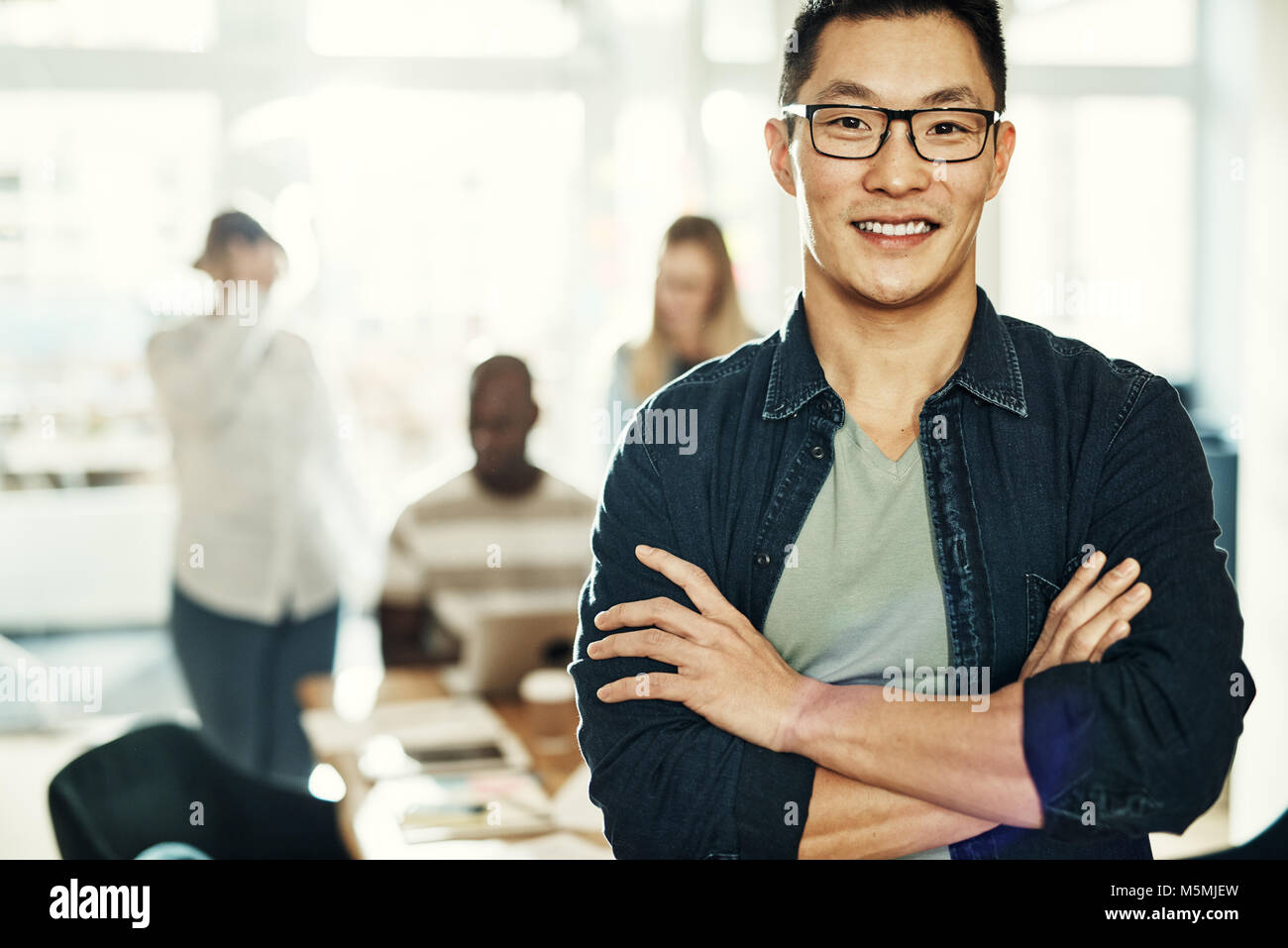 Confident young Asian businessman smiling while standing with his arms ...