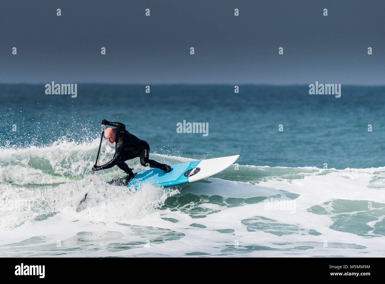 A paddle boarder riding a wave at Fistral in Newquay, Cornwall. Stock Photo