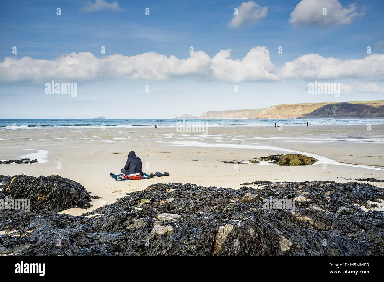 A hooded figure sitting on the beach at Sennen Cove in Cornwall. Stock Photo