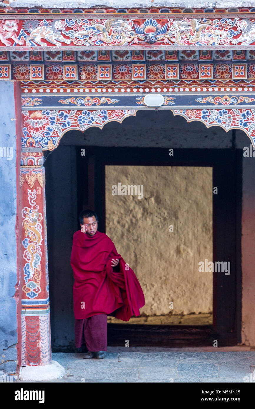 Trongsa, Bhutan.  Young Buddhist Monk Passing through Entryway into First Courtyard of The Trongsa Dzong (Monastery-Fortress), Viewed from Inside the  Stock Photo