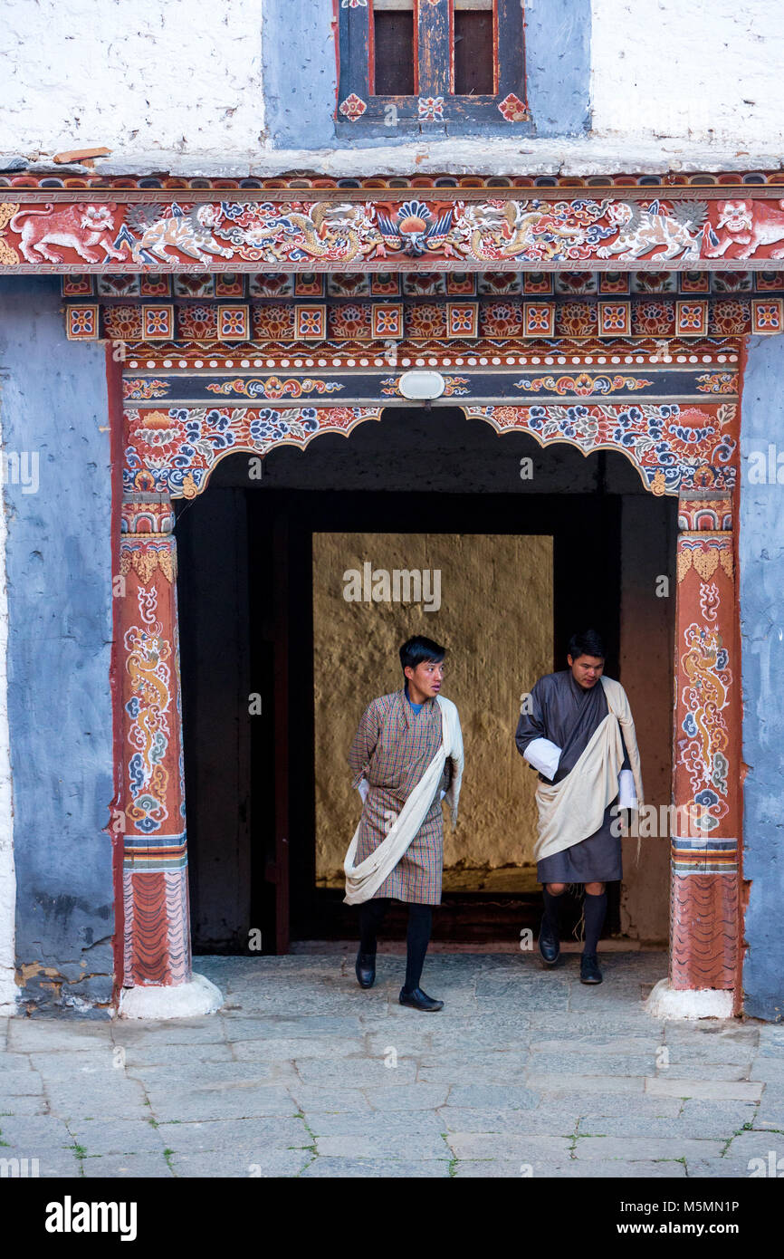 Trongsa, Bhutan.  Two Young Men in Traditional Attire (Gho) Entering First Courtyard of The Trongsa Dzong (Monastery-Fortress), Viewed from Inside the Stock Photo