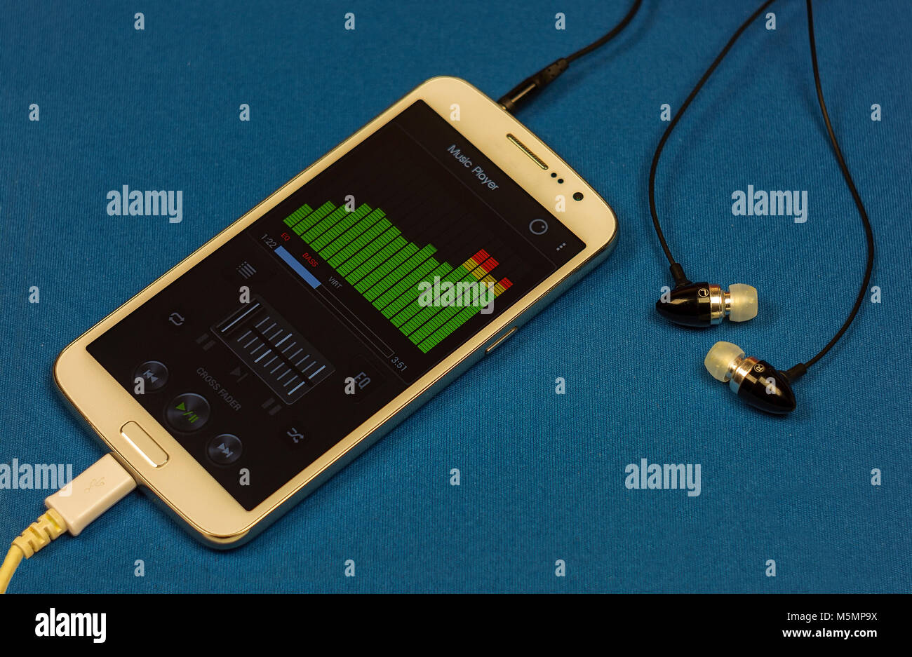 Music player equalizer on smartphone display with headphones, close-up, blue background Stock Photo