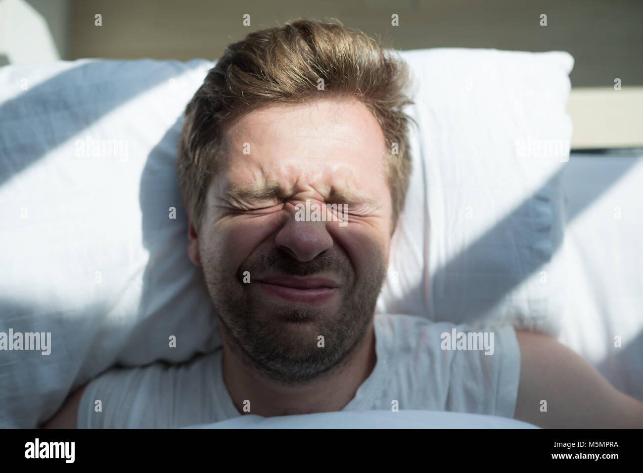 Caucasian mature man in white t-shirt does not want to get up in the morning Stock Photo