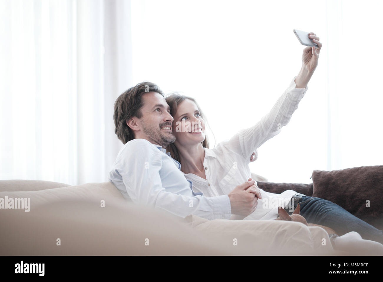 Happy couple taking a selfie together on the couch at home Stock Photo ...