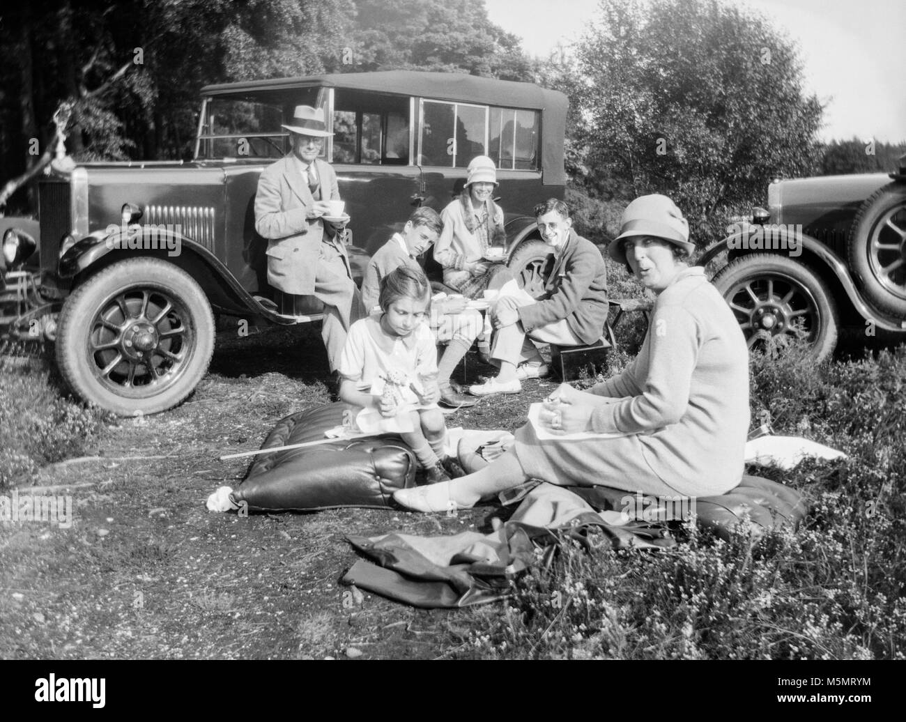 A 1920s image of a family enjoying a picnic with two vintage cars. Stock Photo