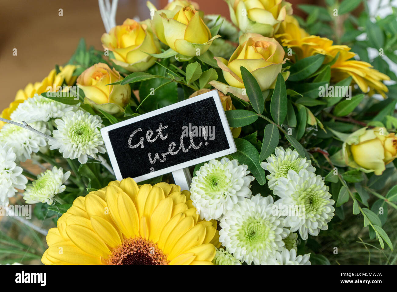 Bouquet of yellow and white roses, gerberas, chrysanthemums and a small board with English text: get well soon Stock Photo