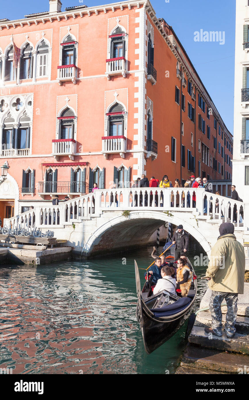 Gondola about to offload tourists in front of the Danieli Hotel, Riva degli Schiavoni, Castello, Venice, Italy with a man waiting with a grappling ho Stock Photo
