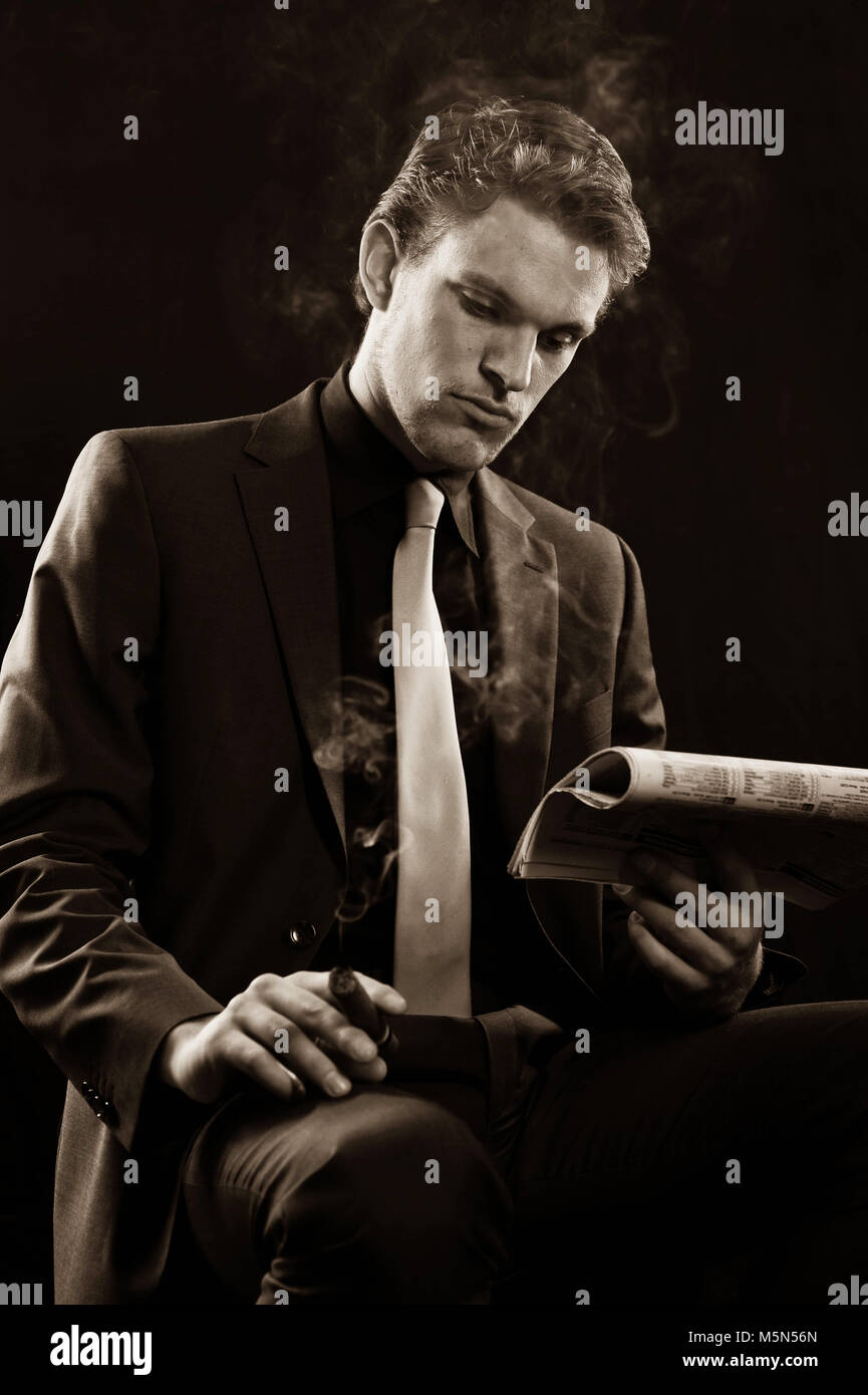 A studio shoot By photographer Claire Allen LRPS in Devizes. A young male model wearing a suit and smoking a cigar. Directional atmospheric lighting. Stock Photo