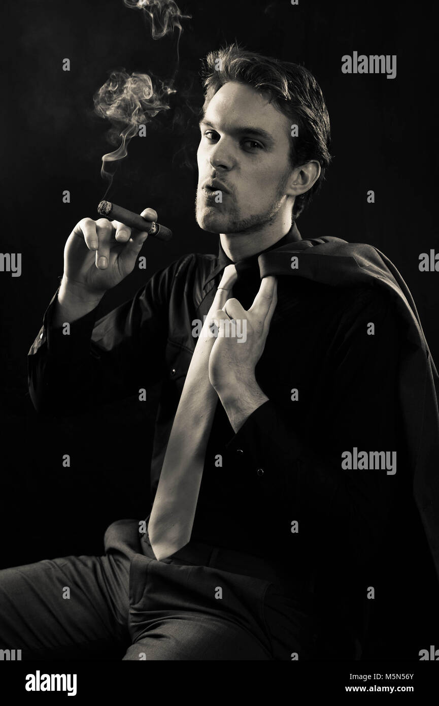 A studio shoot By photographer Claire Allen LRPS in Devizes. A young male model wearing a suit and smoking a cigar. Directional atmospheric lighting. Stock Photo