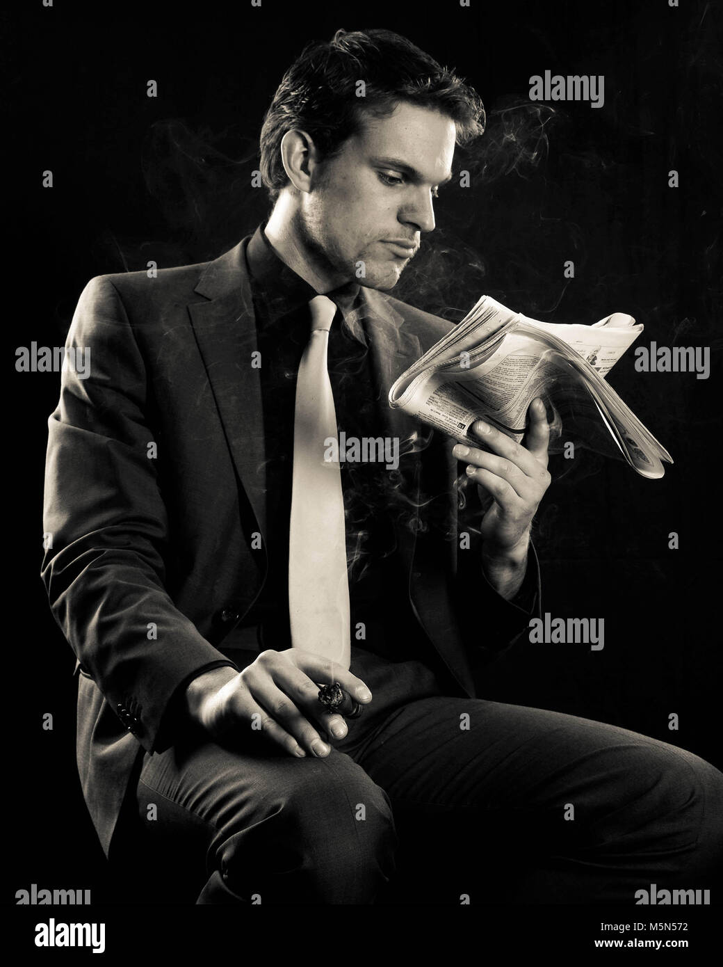 A studio shoot By photographer Claire Allen LRPS in Devizes. A young male model wearing a suit and smoking a cigar. Directional atmospheric lighting. Stock Photo