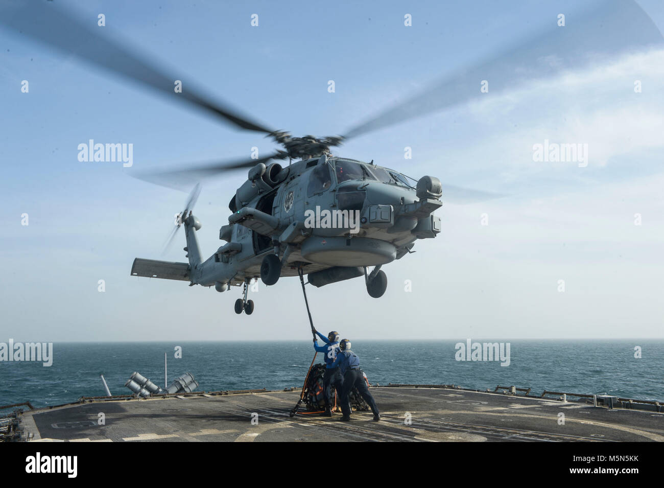 180220-N-VT388-2032 ARABIAN GULF (Feb. 20, 2018) Sailors lift a cargo hook toward an MH-60R Sea Hawk helicopter assigned to the Battlecats of Helicopter Maritime Strike Squadron (HSM) 73, to practice vertical replenishment techniques aboard the guided-missile cruiser USS Bunker Hill (CG 52). Bunker Hill is deployed with the Theodore Roosevelt Carrier Strike Group to the U.S. 5th Fleet area of operations in support of maritime security operations to reassure allies and partners and preserve the freedom of navigation and the free flow of commerce in the region. (U.S. Navy photo by Mass Communica Stock Photo