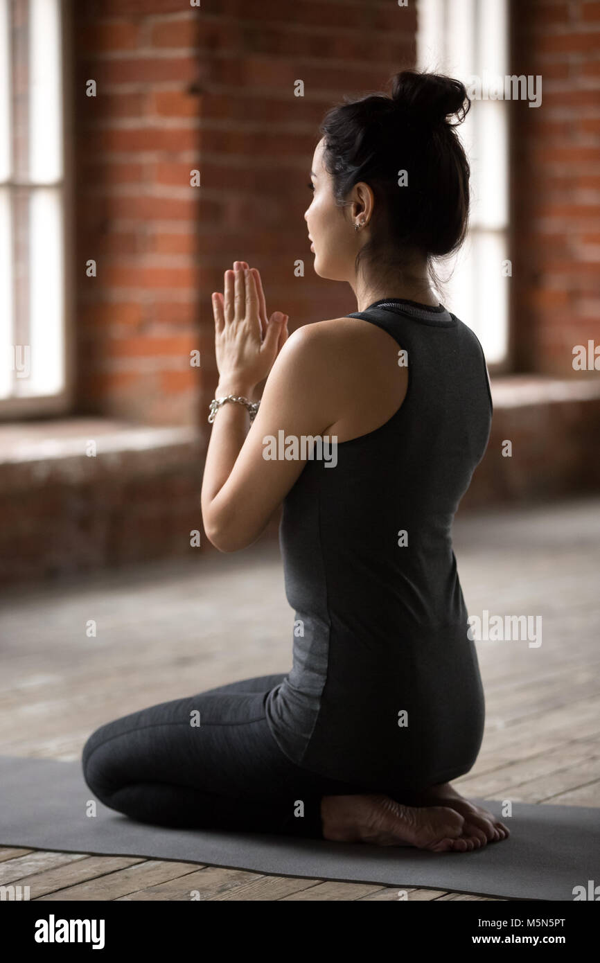 Young woman practicing yoga, doing seiza exercise, vajrasana pose, working out, wearing sportswear, black pants and top, indoor full length, yoga stud Stock Photo