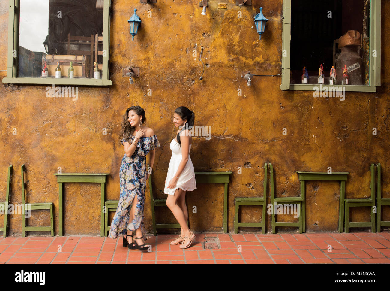 Two young women pose in front of a colorful wall of a bar in Cartagena, Colombia. Stock Photo