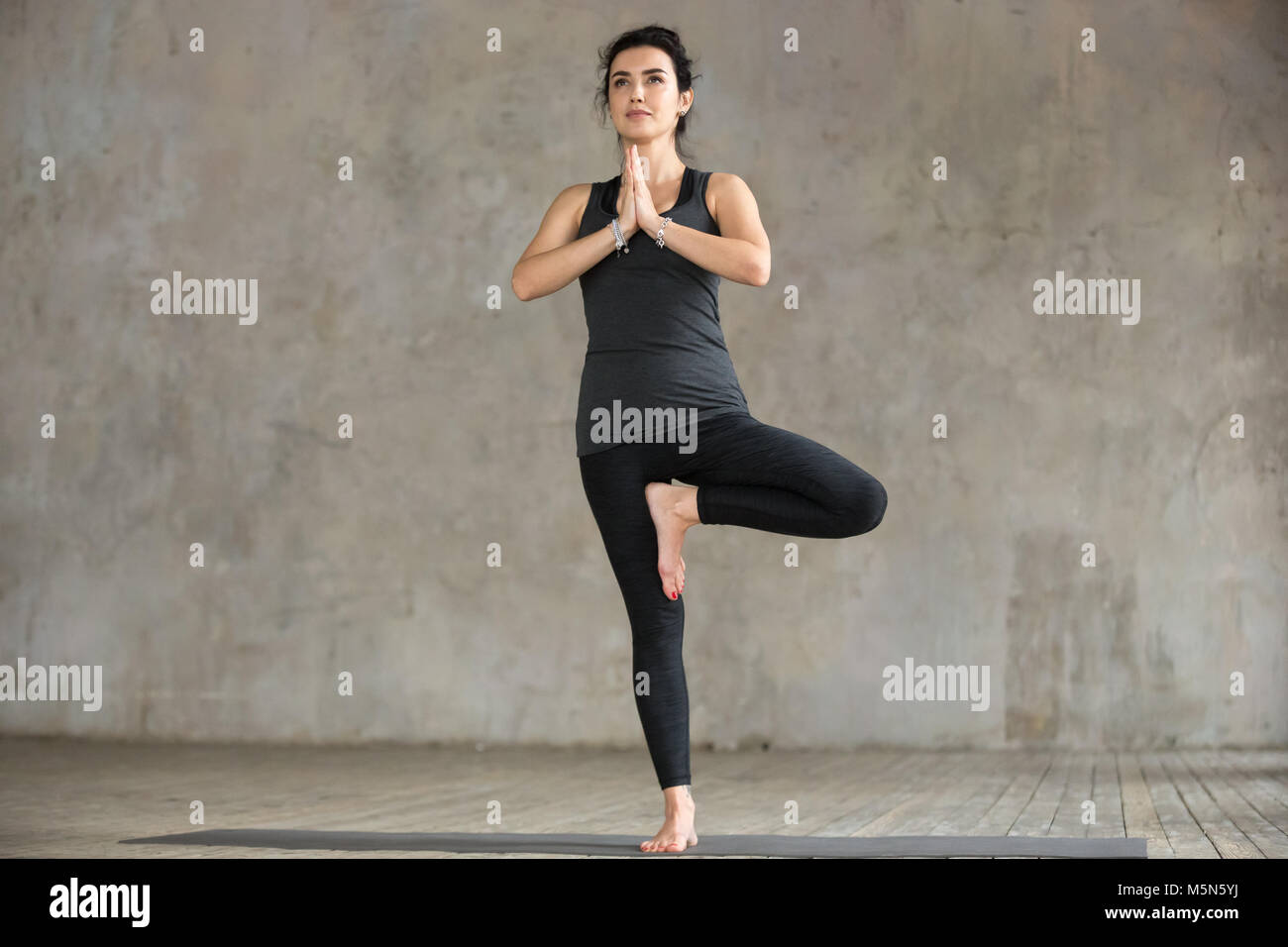 Young sporty woman practicing yoga, doing Vrksasana exercise, Tree pose ...