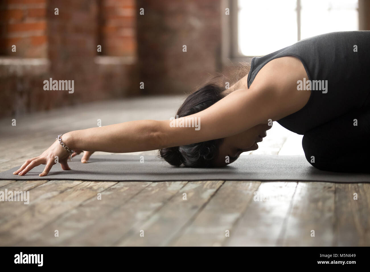 Young sporty woman practicing yoga, doing Child exercise, Balasana pose, working out, wearing black sportswear, indoor close up photo, yoga studio Stock Photo