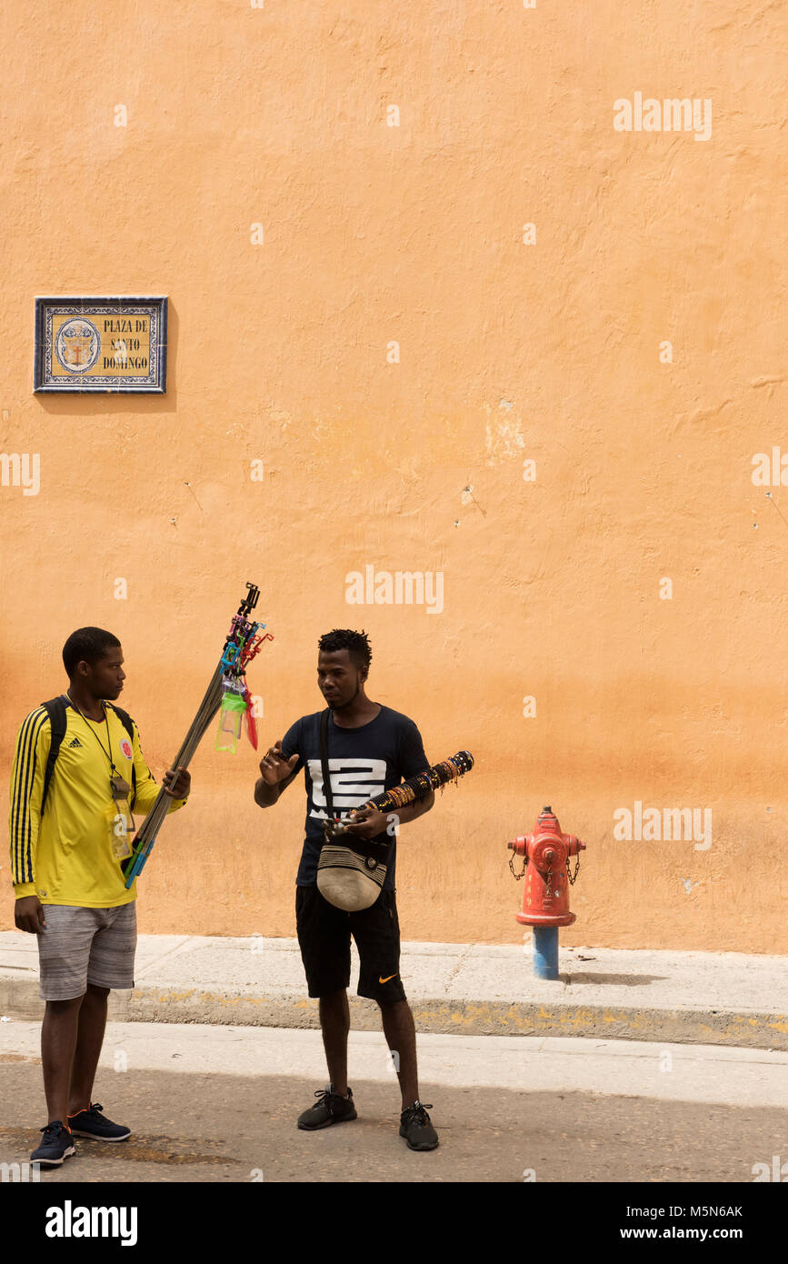 Street sellers talking in Plaza de Santa Domingo, Cartagena with a fire hydrant and street sign against a pink wall Stock Photo
