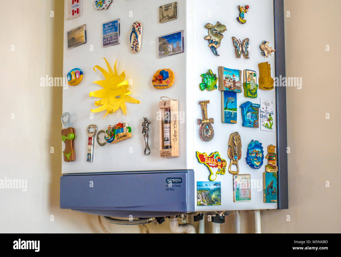 A domestic home gas boiler, for central heating and hot water, wall hung in a room corner, covered in magnetic souvenirs and mementos. England, UK. Stock Photo
