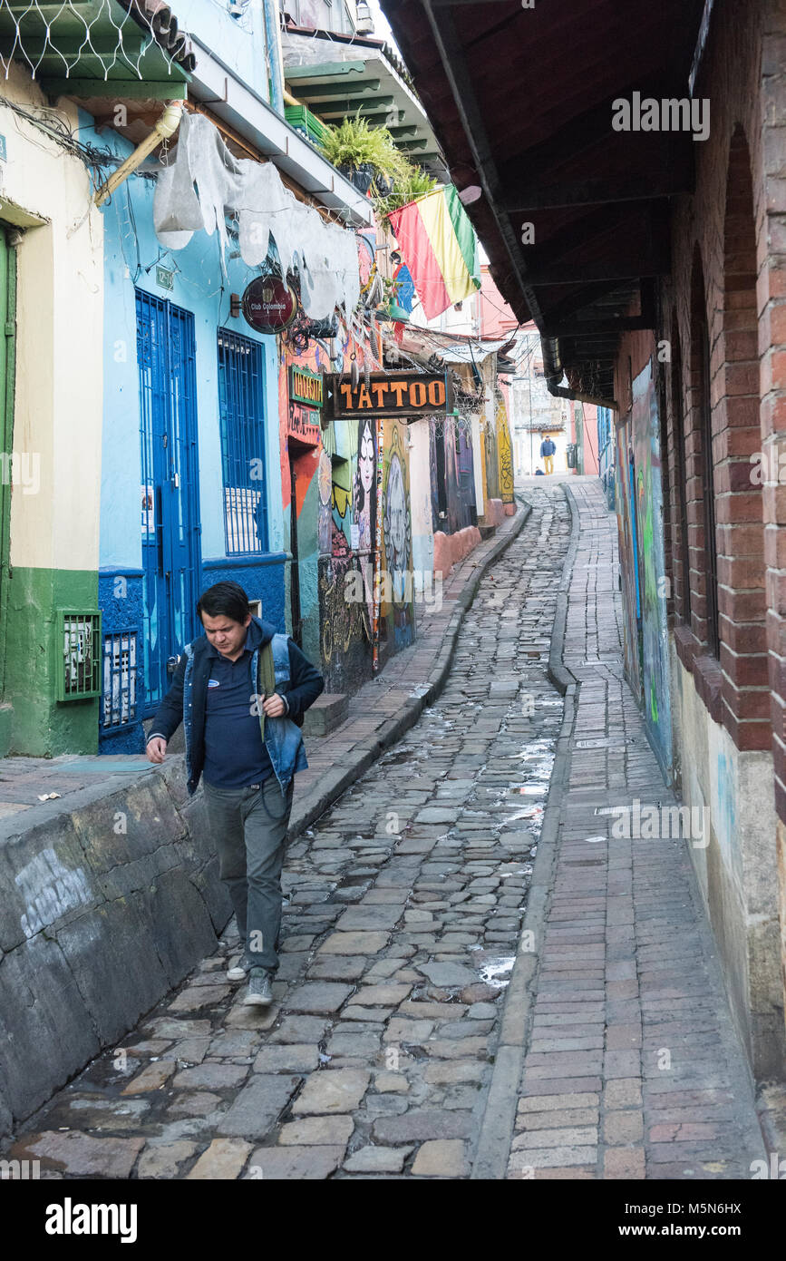 A man walking down a narrow cobbled street in La Candelaria, the vibrant heartbeat of Bogota with some colorful graffiti in the background Stock Photo