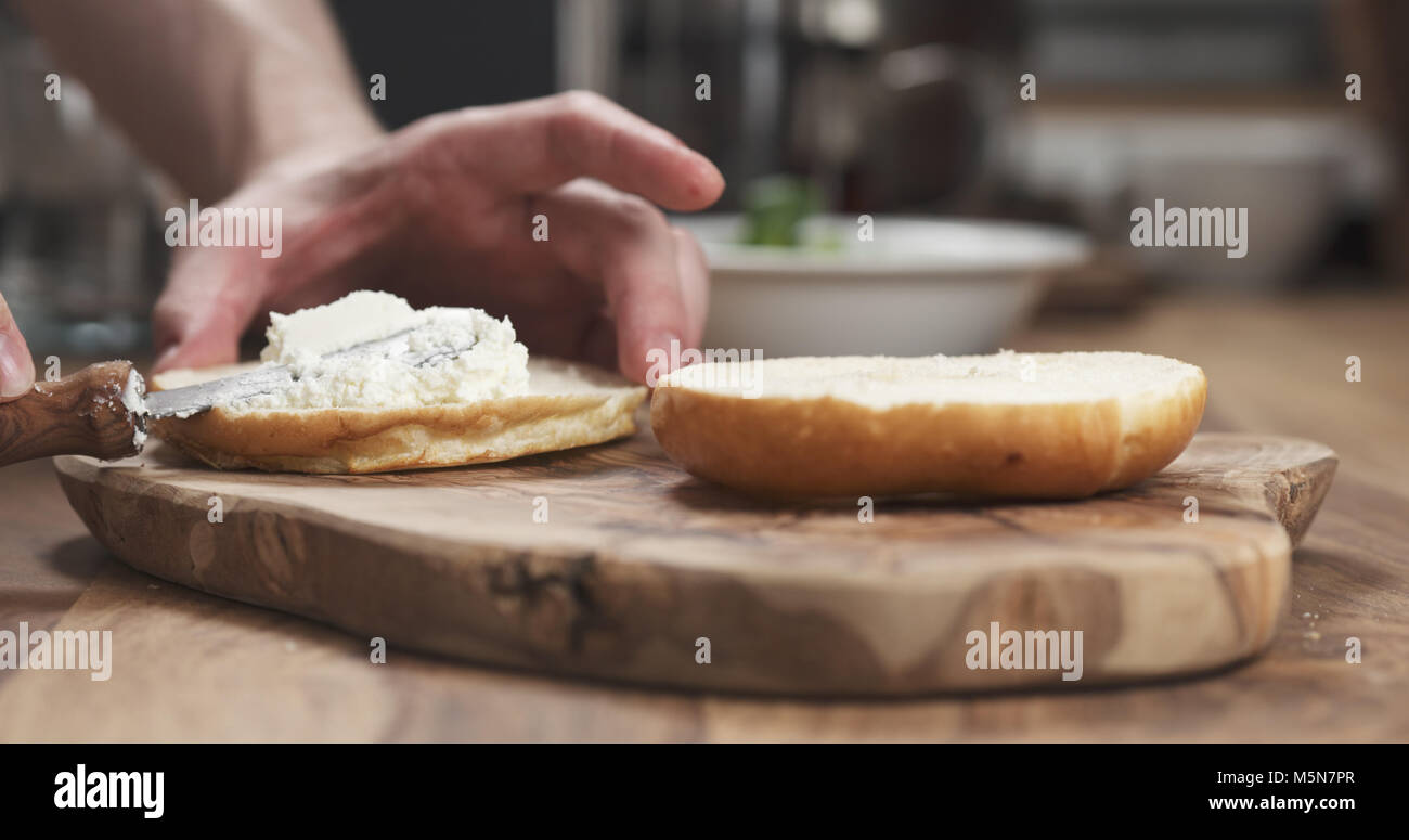 man hands spreading cream cheese on bagel on wood board, wide photo