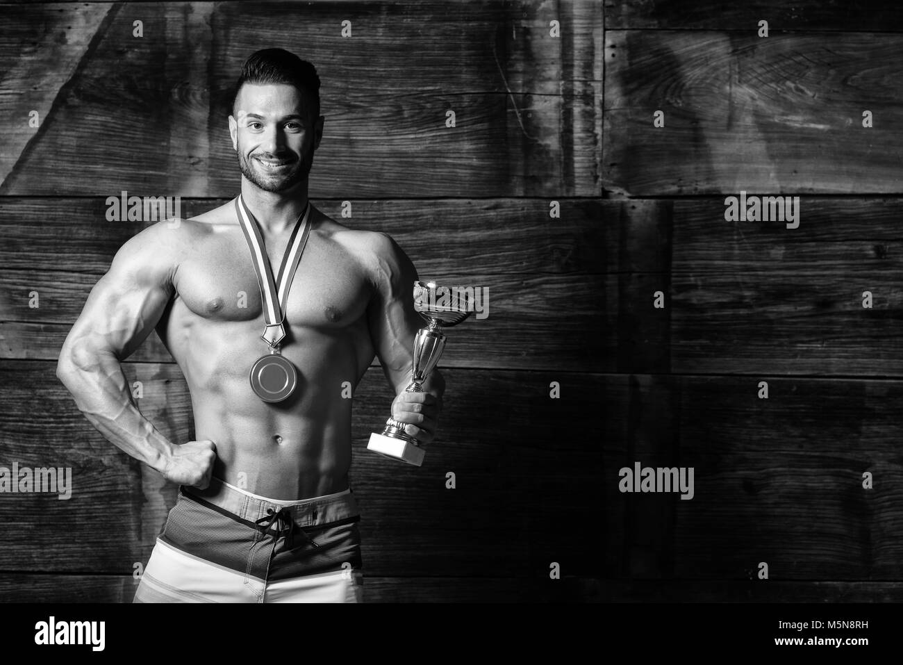Bodybuilder Competitor Showing His Winning Medal Against a Wooden Wall